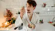 A man in his bathrobe eating oatmeal and fruit in his kitchen.