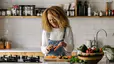 A woman smiling and peeling a carrot in her kitchen to eat more vegetables.