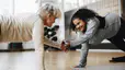 Two people engaging in friendly competition, exercising together and giving each other a high-five while in a plank position on exercise mats.
