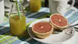 A plate with a grapefruit cut in half next to a bottle of fresh orange juice, both of which are hydrating foods and drinks.