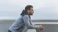 How to Change Your Mindset: A young man leaning his arms on a ledge while looking out thoughtfully at the sea.