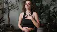 A woman practicing belly breathing. She is sitting tall with one hand on her chest and one hand on her belly, her eyes closed.