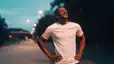 A man recovering from an outdoor walk or jog at night while looking up at the sky and putting his hands on his hips. 