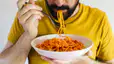 A close-up photo of a man eating a bowl of spaghetti as he eats before a marathon.