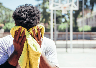 A man wiping away sweat from his face with a clean towel after an outdoor basketball game to prevent sweat pimples.