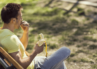 A man sitting on a park bench and eating a banana before a workout.