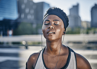 Why Do I Sweat So Much? - Image of a woman closing her eyes and standing outside sweating after a workout.
