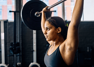 A woman doing an overhead press with a barbell in the gym.