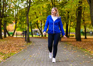 A woman walking after eating. She's going for an outdoor walk in a local park.