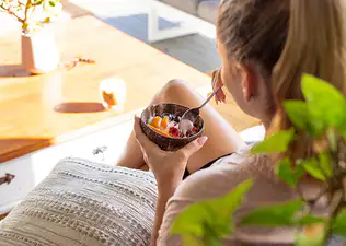 A runner eating a yogurt parfait with fruit after a run while sitting on the couch at home.