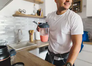 A close-up photo of a man drinking a smoothie in his kitchen, a great post-workout recovery drink.