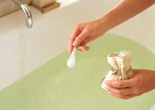 A close-up photo of a person sprinkling Epsom salt into a bath.