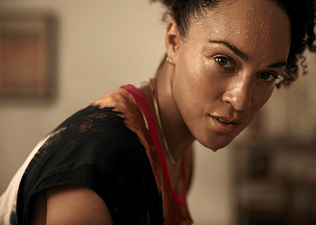 In this image for an article about high-performance mindsets, a woman is looking powerfully into the camera. She's sweaty and has her hair up.