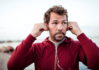 A man holding his ears and adjusting his headphones as he pauses his outdoor run. His ears are hurting while running.
