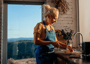 A middle-aged woman making mindful menopause nutrition choices by making a healthy salad. She's standing in her modern kitchen and chopping an onion.
