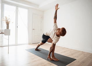 A man doing yoga before or after a workout. He's doing Triangle Pose on a yoga mat at home.