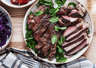 A plate of cooked steak cut up and arranged on a plate with greens. Learn how much protein is too much in this article.