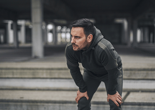 A man catching his breath after a run, with his hands on his knees. He is not hungry after his workout.