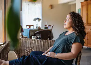 A woman sitting in her home, closing her eyes, and calmly manifesting something.
