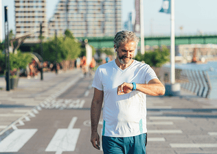 A man looking at his sports watch while walking outside for five minutes.