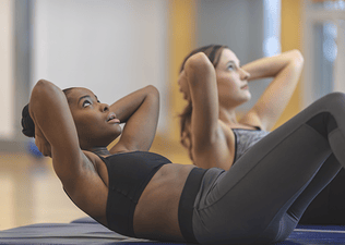 Two women do crunch exercises at the gym
