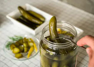 A close-up photo of someone using a fork to take a pickle out of a pickle jar.