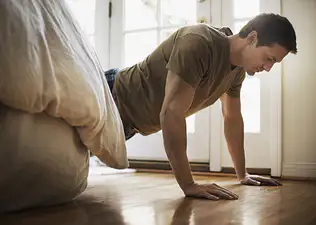 A man doing push-ups before bed. He is in a high plank position next to his bed.