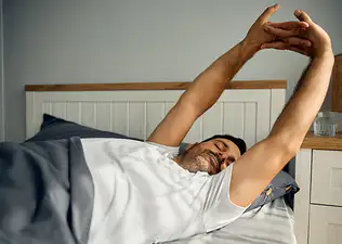 A man waking up stress-free after a night of rest on his consistent sleep schedule.