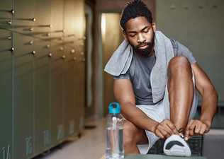 A man lacing up his running shoes in a locker room before going to work out.