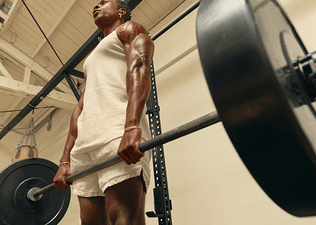 Muscular young man doing a barbell deadlift in front of a squat rack in the gym