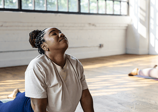 Woman doing easy yoga poses during a yoga class in a bright room on wood floors.