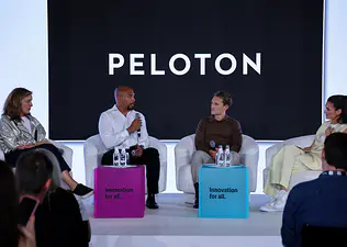 Four panelists seated on stage during a Peloton event in front of a backdrop displaying the Peloton logo.