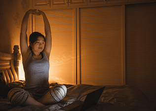 Woman stretches while sitting on bed