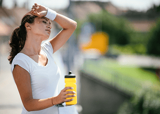 A tired athlete rubbing sweat off her forehead with her sweatband and drinking from a yellow water bottle. Learn how to rehydrate in this article.