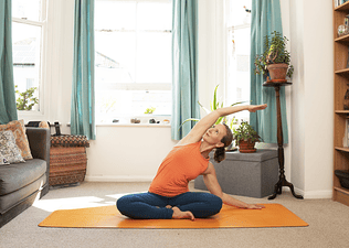 Woman doing seated side bend oblique stretch at home on a yoga mat