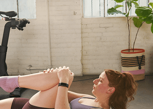 Young woman doing Pilates on an exercise mat next to a Peloton Bike