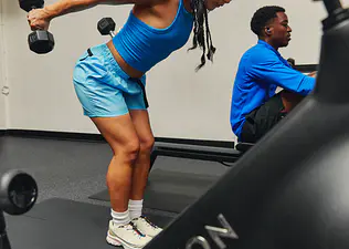 Young woman doing the triceps kickbacks exercise with proper form in a gym next to a Peloton Bike