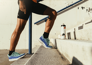 Runner standing on a staircase outside doing calf stretches and calf raises.