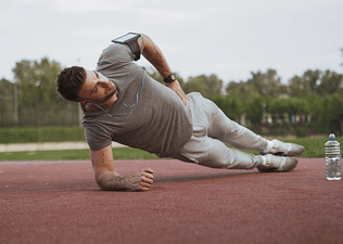 Man in gray t-shirt and sweatpants doing a side plank outside 