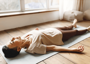 A woman in Savasana pose on her yoga mat at home.