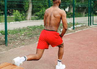 Man doing Bulgarian split squats on a park bench during a no-equipment full body workout.