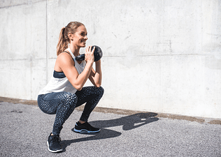 Woman does sumo squat while holding a kettlebell 