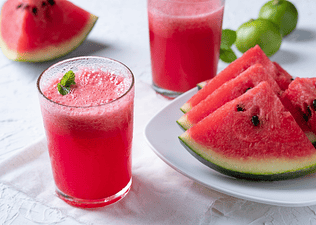 A glass of watermelon juice garnished with fresh mint leaves sitting next to a plate of other watermelon slices.