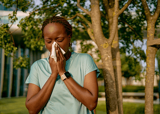 A woman blowing her nose into a tissue during an outdoor workout. She's exercising with allergies.