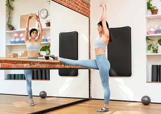 Woman doing barre exercise in studio with arms in air and leg on barre