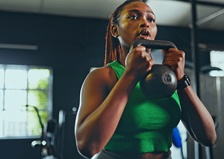 Woman holding a kettlebell in front of her chest while doing kettlebell arm exercises in a gym.