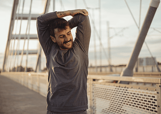 A man smiling and stretching his arms before going on an outdoor run in the morning.