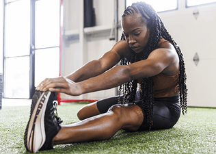 Young woman stretching to build muscle in a gym setting.