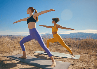 Two women in Peloton apparel doing yoga outside in a desert reaping the mind and body benefits of yoga.
