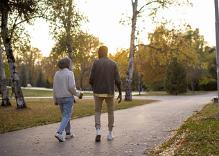 A back view of a couple going on a "fart walk" through an outdoor park on an autumn evening.
